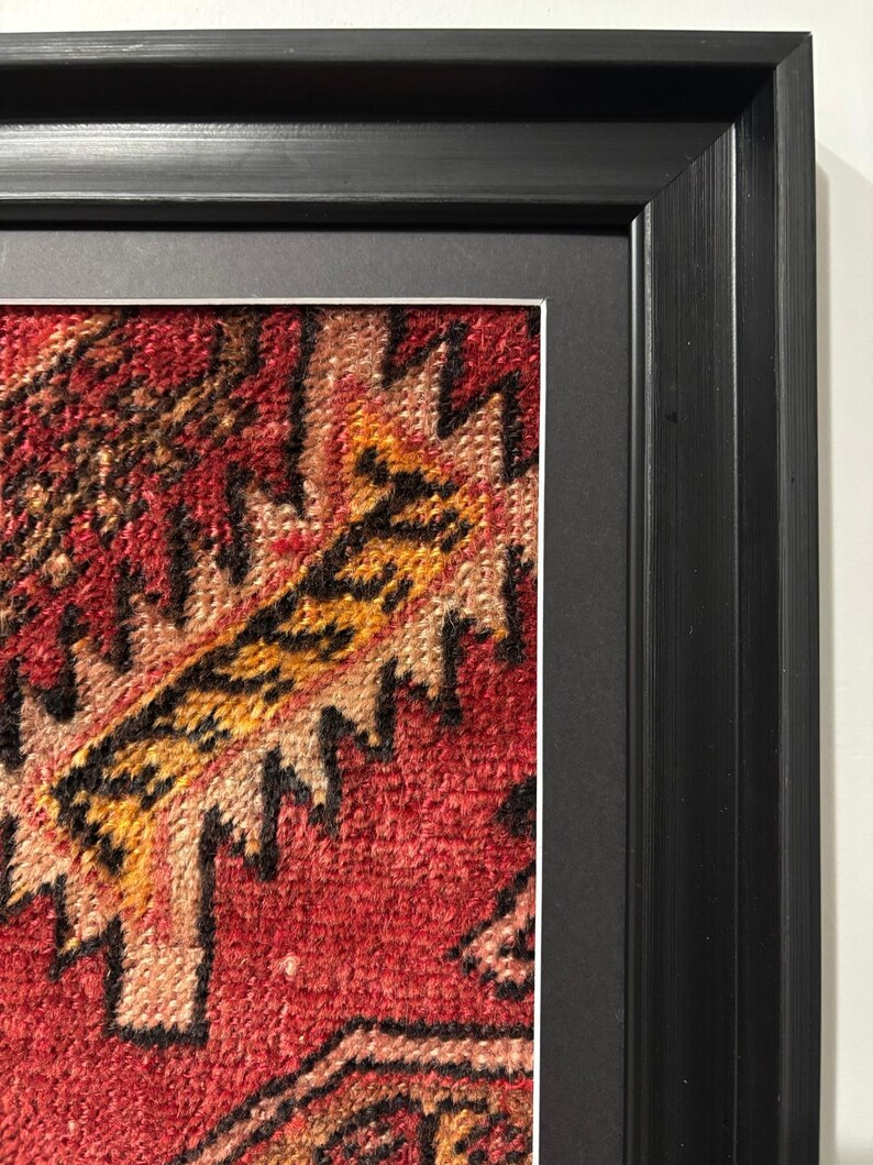 Pode incluir: Close-up de uma obra de arte t&ecirc;xtil emoldurada. A obra apresenta um padr&atilde;o intrincado e vibrante em tons de vermelho, amarelo e preto. A moldura &eacute; um design retangular preto simples, proporcionando uma borda limpa para a obra de arte.