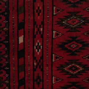 Puede incluir: Una pieza textil enmarcada con un fondo rojo intenso y complejos patrones geom&eacute;tricos en negro y blanco. La tela se exhibe dentro de un paspart&uacute; negro y un marco de madera blanca, mostrando rayas verticales y motivos en forma de diamante.