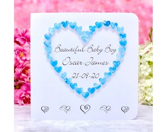 Può includere: Un biglietto bianco con un cuore blu fatto di cuori piccoli. Il biglietto dice "Beautiful Baby Boy Oscar James 21-09-20".