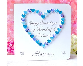 Può includere: Un biglietto bianco con un cuore blu e viola fatto di piccoli cuori di carta. Il biglietto dice "Happy Birthday to my Wonderful Husband Alastair".