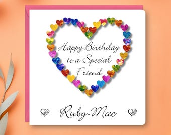 Può includere: Un biglietto d'auguri quadrato bianco con una forma a cuore composta da piccoli cuori multicolori a motivi. All'interno del cuore, il testo recita Happy Birthday to a Special Friend. Sotto il cuore, il nome Ruby-Mae in corsivo nero.