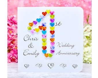 Può includere: Un biglietto bianco con un design a forma di cuore colorato che forma il numero 41. Il testo "Chris & Emily 41° Anniversario di Matrimonio" è stampato sulla carta.