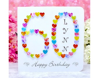 Può includere: Un biglietto bianco con il numero 60 fatto di cuori colorati. Il numero 60 è circondato dal nome Lynn. Il biglietto dice "Buon compleanno" in basso.