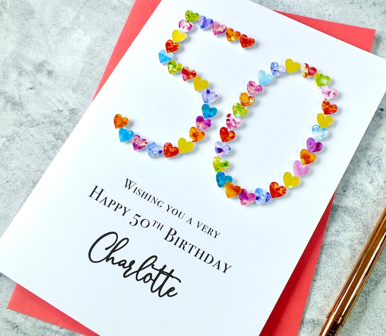 May include: A white card with the number 50 made out of colorful hearts. The text "Wishing you a very happy 50th birthday Charlotte" is printed on the card.