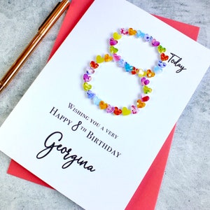 May include: A white card with a colorful number eight made of hearts. The card says "Wishing you a very happy 8th birthday Georgina" and "Today".