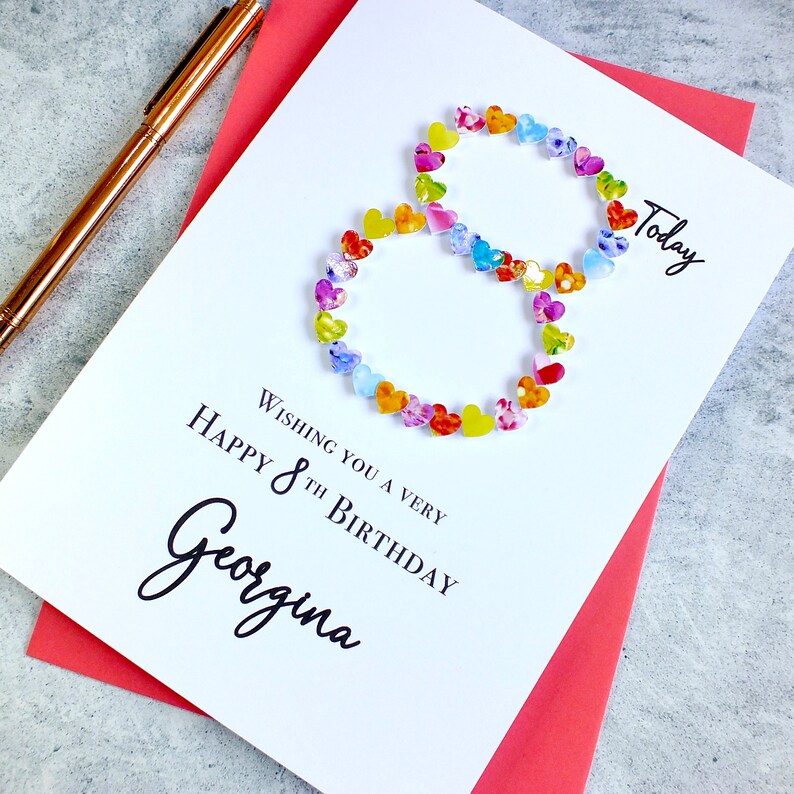 May include: A white card with a colorful number eight made of hearts. The card says "Wishing you a very happy 8th birthday Georgina" and "Today".