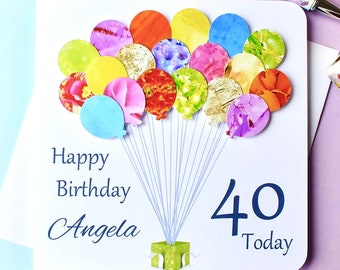 Può includere: Un biglietto bianco con un design blu e bianco. Il biglietto ha un mazzo di palloncini colorati con una scatola regalo in fondo. Il testo sul biglietto dice "Buon compleanno Angela 40 Oggi".