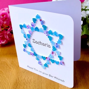 May include: A white card with a blue and purple heart design. The card says "Zacharia Mazel Tov on your Bar Mitzvah".
