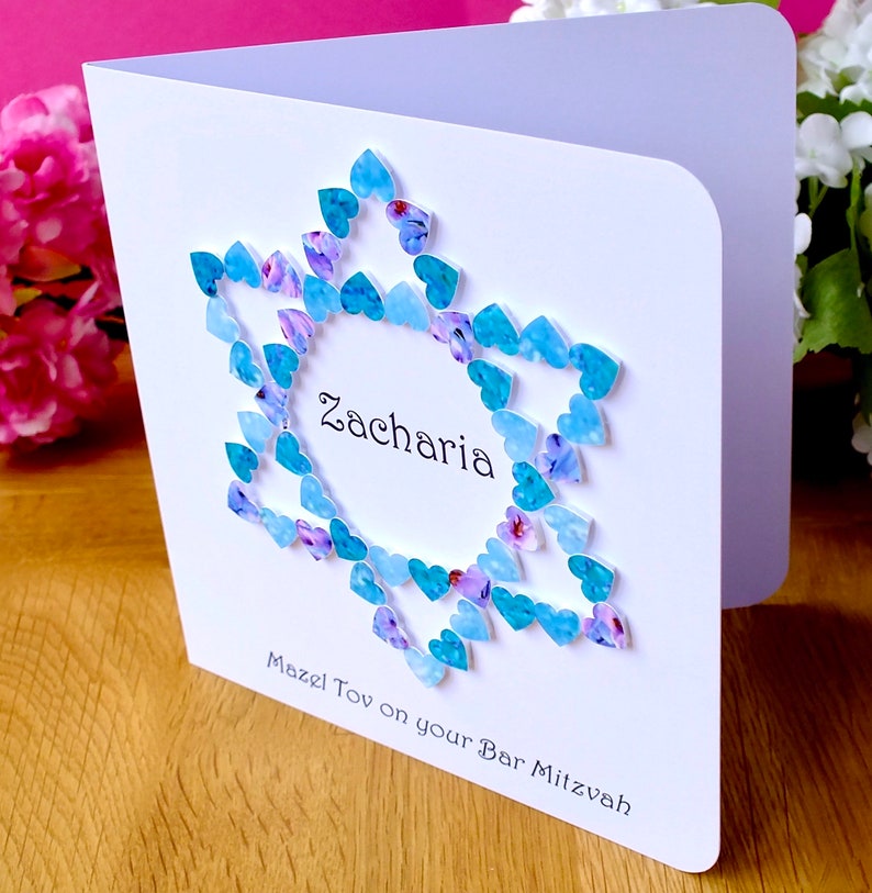 May include: A white card with a blue and purple heart design. The card says "Zacharia Mazel Tov on your Bar Mitzvah".