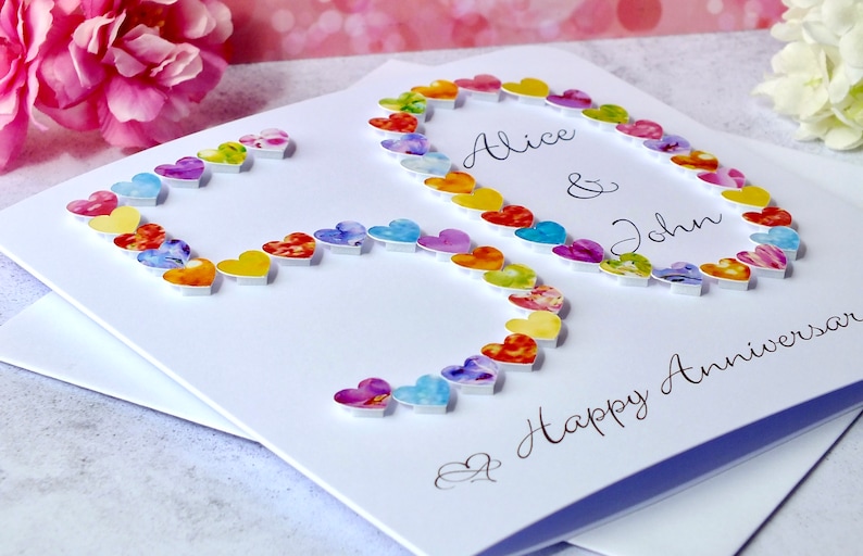May include: A white card with a colourful heart design spelling out the number 50. The card says "Alice & John" and "Happy Anniversary".