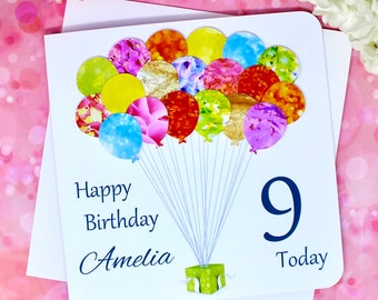 Può includere: Un biglietto bianco con un design di palloncini blu e bianchi. Il biglietto dice "Buon compleanno Amelia 9 Oggi".