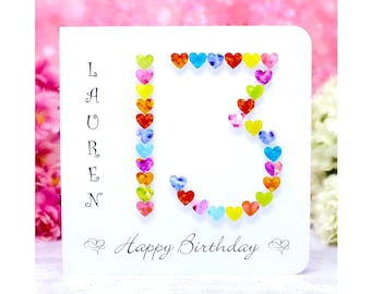 Può includere: Un biglietto d'auguri bianco con il nome LAUREN scritto verticalmente in nero, il numero 13 formato da piccoli cuori multicolori e la scritta Happy Birthday in basso con decorazioni floreali su entrambi i lati della frase.