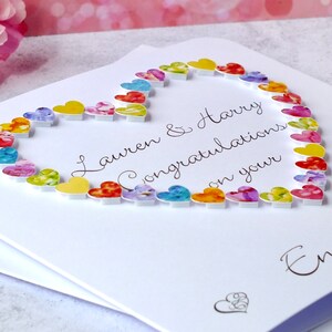 May include: A white card with a heart made of colorful paper hearts. The card says "Lauren & Harry Congratulations on your Engagement".