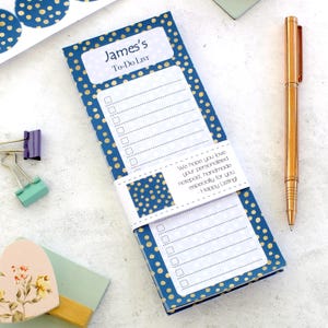 May include: A blue notepad with gold polka dots, labelled "James's To-Do List". The notepad is held together with a white band. A gold pen and stationery items are also visible. The notepad is for making lists.