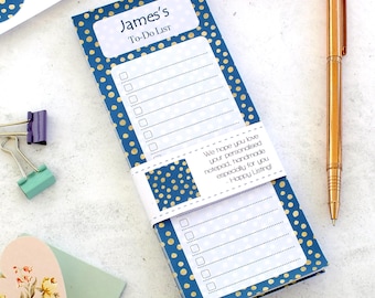 Può includere: Un blocco note personalizzato con lista di cose da fare, sfondo blu a pois dorati. Porta la scritta "James's To-Do List". Sono visibili anche una penna dorata e altri articoli di cancelleria.