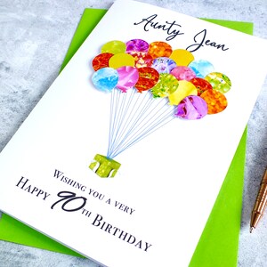 May include: A white card with a colorful balloon design and the text "Wishing you a very Happy 70th Birthday" and "Aunty Jean".