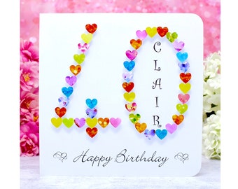 Può includere: Un biglietto bianco con un design a forma di cuore colorato che compone il numero "40" e il nome "Clair". Il biglietto dice anche "Buon compleanno".