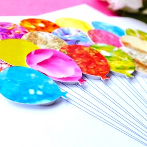 May include: A cluster of colorful balloons with various patterns, including floral, abstract, and geometric designs. The balloons are tied together with strings and are arranged in a semi-circle.