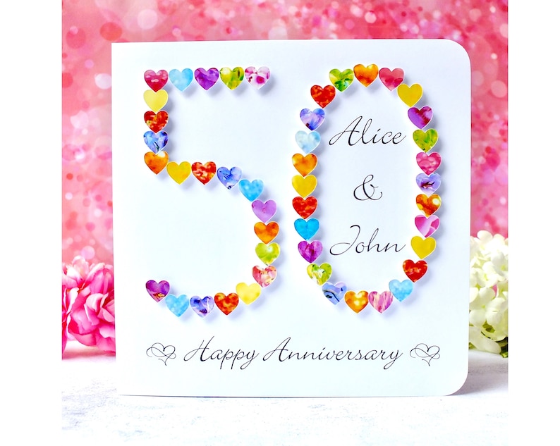 May include: A white card with the number 50 made of colourful hearts. The card says "Alice & John Happy Anniversary" in black script.