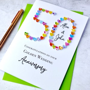 May include: A white card with the number 50 made out of colourful hearts. The card says "Congratulations on your Golden Wedding Anniversary" and "Alice & John".