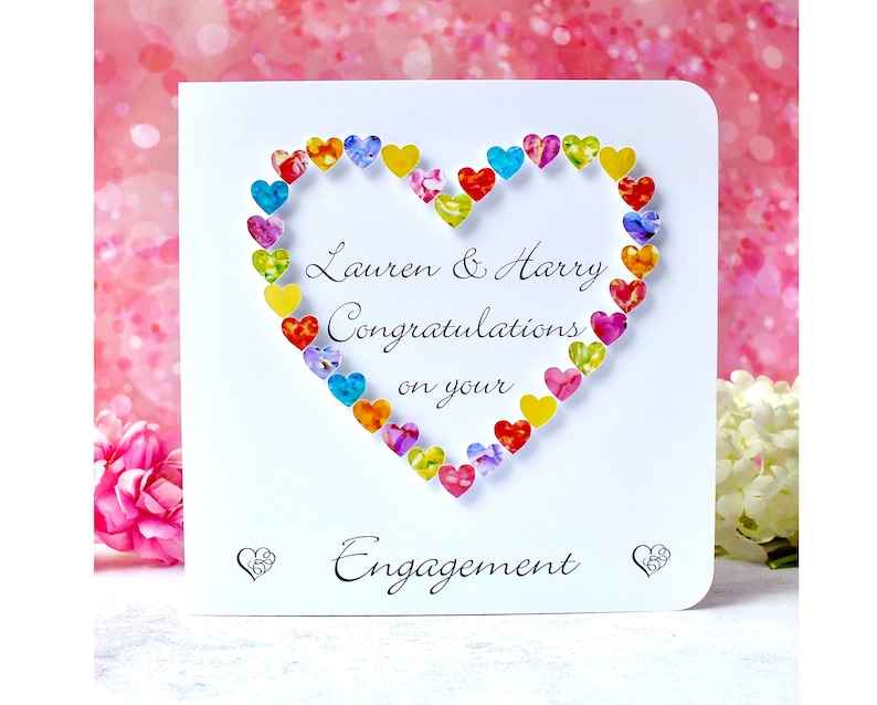 May include: A white card with a heart made of colorful paper hearts. The card says "Lauren & Harry Congratulations on your Engagement".