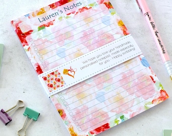Può includere: Blocco note con motivo floreale rosa e bianco con la scritta "Lauren's Notes". Una penna rosa con la scritta "You're better than unicorns" è accanto al blocco note. Il blocco note è tenuto insieme da una fascia bianca con testo.