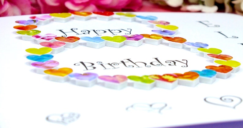 May include: A white card with the words "Happy Birthday" written in black cursive. The number eight is formed with a circle of colorful hearts.