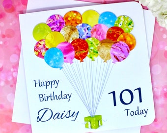 Può includere: Un biglietto bianco con un design di palloncini colorati. Il biglietto dice "Happy Birthday Daisy 101 Today".