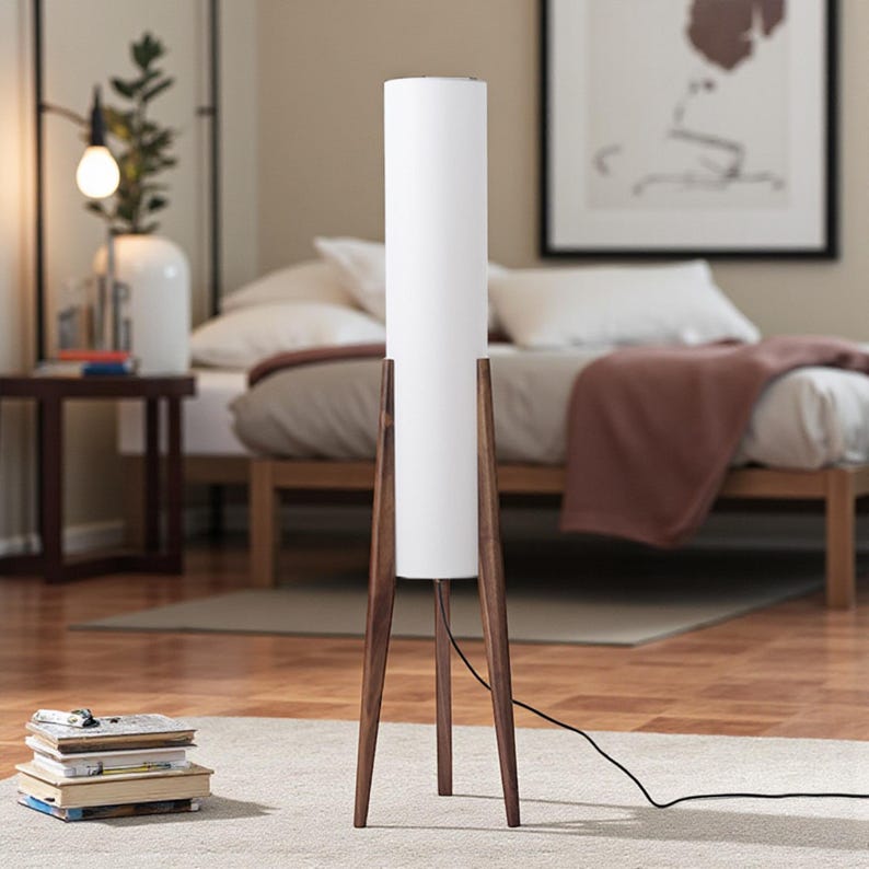 May include: A modern floor lamp with a white cylindrical shade and a dark brown wooden tripod base. The lamp is tall, standing on a light-colored rug in a bedroom setting. The lamp's height is approximately 60 inches.