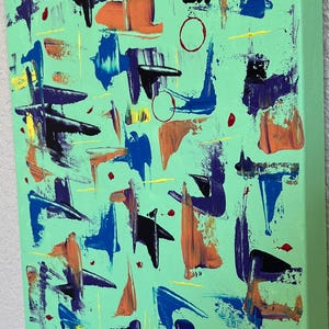 May include: A rectangular canvas painting featuring a light mint green background with scattered abstract brushstrokes in shades of royal blue, deep purple, bright orange, and yellow, accented by small red dots and thin circular outlines.