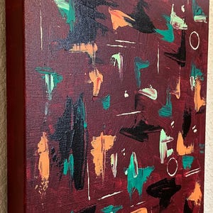 May include: A rectangular canvas painting featuring a deep burgundy background with abstract brushstrokes in black, bright orange, teal, and pale green. The composition includes thin white linear marks and small hand-painted circles scattered across the surface.