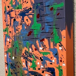May include: A rectangular canvas painting featuring an orange background layered with abstract brushstrokes in blue, green, black, white, and dark red. The paint application includes thick horizontal lines, splatters, and drips across the surface.