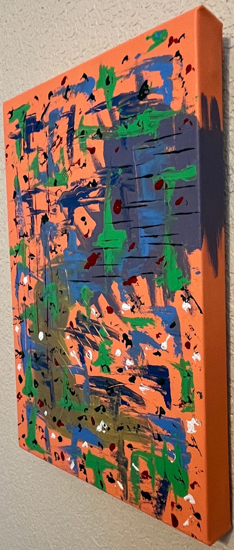 May include: A rectangular canvas painting featuring an orange background layered with abstract brushstrokes in blue, green, black, white, and dark red. The paint application includes thick horizontal lines, splatters, and drips across the surface.