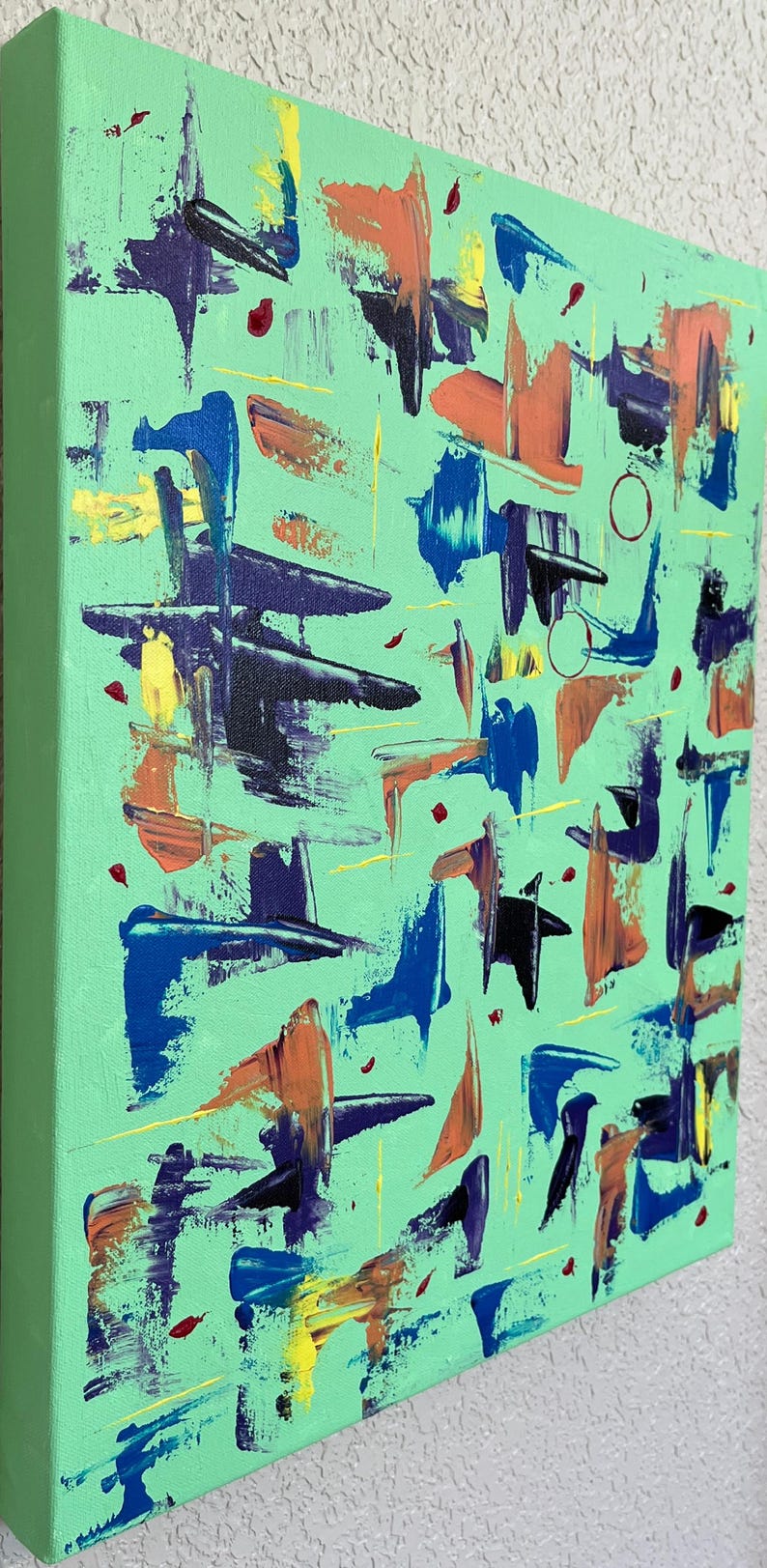 May include: A rectangular canvas painting featuring a light mint green background with abstract brushstrokes in shades of dark blue, orange, yellow, and purple. The composition includes scattered paint dabs and thin lines across the surface.