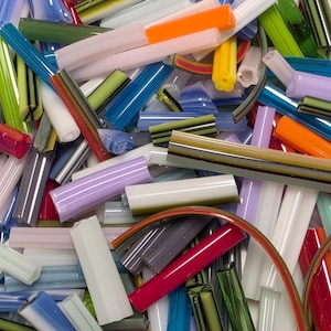 May include: A collection of colorful glass rods and tubes in various shapes and sizes. The assortment includes shades of red, blue, green, orange, and white, with some pieces featuring striped patterns. The pieces are scattered, creating a visually appealing display.