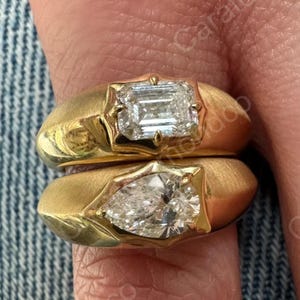 Peut inclure: Deux bagues en or, l'une avec un diamant taille émeraude et l'autre avec un diamant en forme de poire. Les bagues ont une finition brossée. Fond en jean.