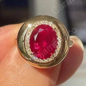 Peut inclure: Une bague en or ornée d'un grand rubis ovale. Le rubis est entouré d'un halo de petits diamants étincelants. La bague présente un design classique et élégant.