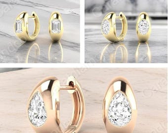 May include: Gold hoop earrings with a clear, rectangular-cut stone. The earrings have a polished finish and a secure clasp. The earrings are displayed on a marble surface.
