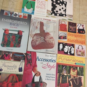 May include: A collection of books on bag making and accessories. Titles include "Handmade Embroidered Bags", "Duct Tape Bags", "Hip Handbags", "Making Vintage Bags", "Designer Style Handbags", "Pursenality Plus", "Accessories with Style", and "Crocheted Pursenalities".