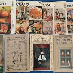May include: A collection of craft pattern books featuring various seasonal themes. The covers display images of pumpkins, Christmas decorations, and other holiday-themed crafts. The books are arranged on a blue surface.