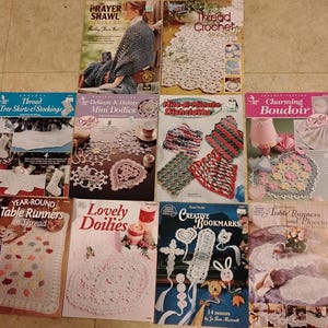 May include: A collection of crochet pattern books featuring various designs. Titles include "Prayer Shawl", "Thread Crochet", "Tree Skirts & Stockings", "Mini Doilies", "Charming Boudoir", "Table Runners", and "Creative Bookmarks". The books showcase intricate crochet projects.