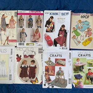 May include: A collection of eight sewing patterns for baby and children's clothing and accessories. The patterns include a variety of styles, such as dresses, rompers, and blankets. The patterns are printed on white paper with black and red text. The patterns are from McCall's and Simplicity.