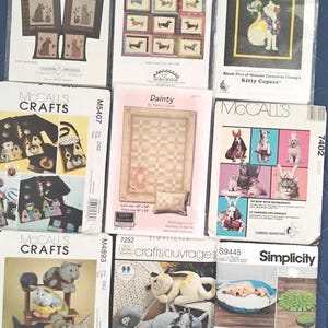 May include: A collection of sewing pattern packets featuring dogs and cats. The packets display various projects, including stuffed animals, quilts, and apparel. Some packets have text like "Good Dog! Nice Cat!" and "Hot Diggity Dog!"