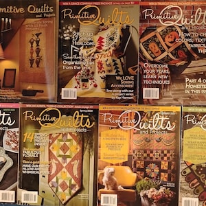 May include: A collection of "Primitive Quilts and Projects" magazines. The covers feature quilts, seasonal themes, and articles on quilting techniques. The magazines are displayed on a blue surface.