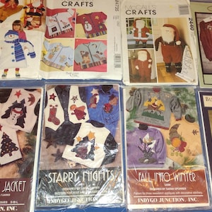 May include: A collection of 10 different craft patterns featuring winter-themed designs. The patterns include a cotton bale jacket, starry nights, fall into winter, button on banners, and snowman sweater. The patterns are printed on white paper with colorful illustrations.