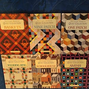 May include: A collection of six books titled "The Classic American Quilt Collection." The book covers feature quilt patterns such as "Baskets," "Nine Patch," "One Patch," "Wedding Ring," "Schoolhouse," and "Amish." The books are arranged on a blue surface.