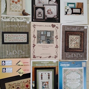 May include: A collection of cross stitch patterns featuring various themes, including words to stitch by, thoughts of wisdom, samplers, and room in the heart. The patterns are printed on colorful paper with a variety of designs and fonts.