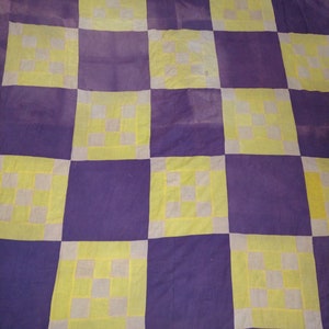 May include: A handmade quilt with a checkerboard pattern. The quilt features alternating squares of deep purple and light yellow. Each yellow square contains a smaller square pattern in white and light yellow.
