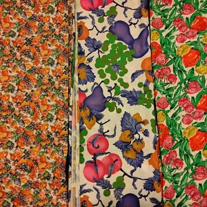 May include: Three fabric swatches with colorful fruit patterns. One features oranges and grapes, another has pears, grapes, and strawberries, and the third showcases red and yellow fruits with green leaves. The fabrics have a vintage aesthetic.
