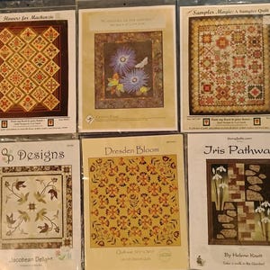 May include: A collection of quilt patterns in plastic sleeves. The patterns feature various designs, including floral arrangements, geometric patterns, and a sampler quilt. The patterns are labeled with titles such as "Flowers for Mackenzie" and "Dresden Bloom."